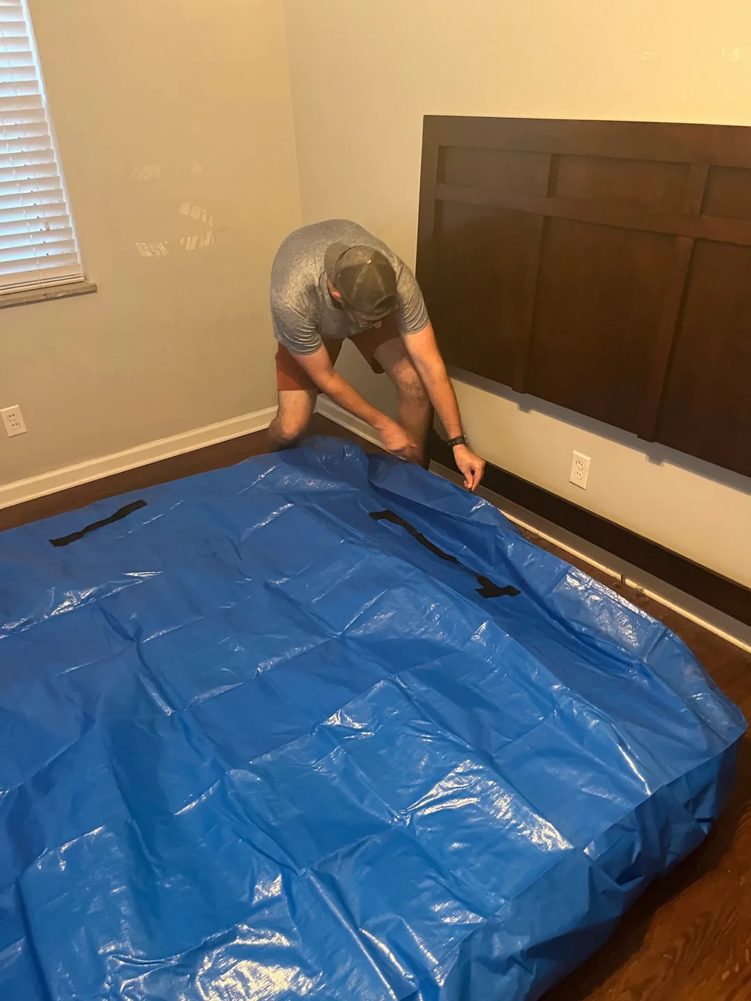 A crew member fitting a protective blue cover over a large item inside a residence