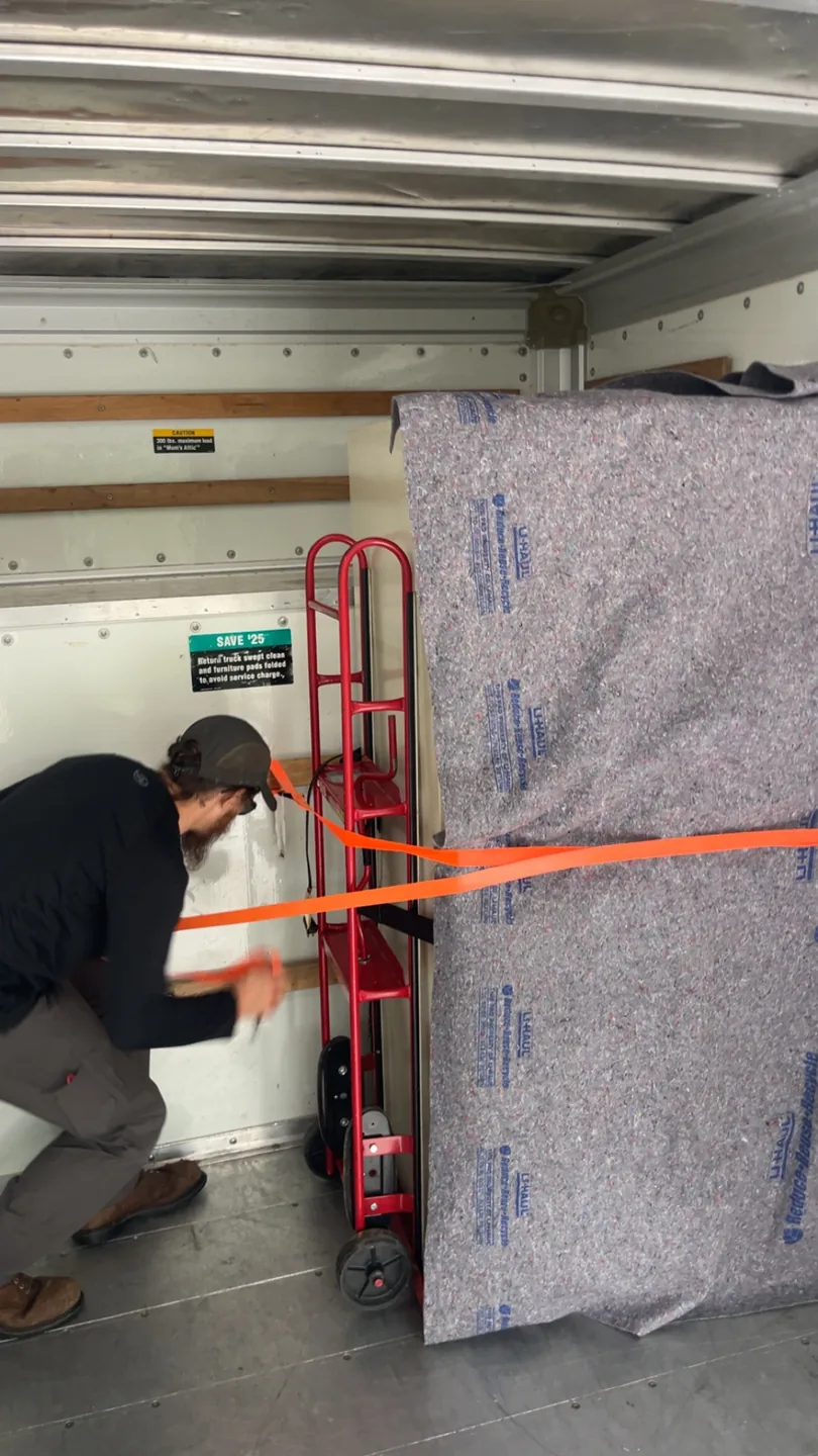A crew member securing a blanket-protected item inside a box truck